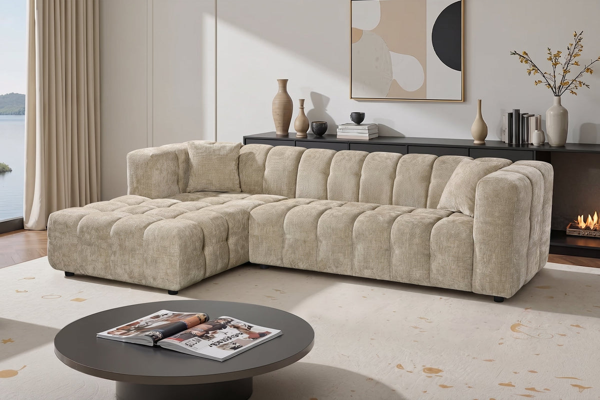 An L-shaped tufted sofa with left hand facing chaise end section, upholstered in beige chenille fabric, styled in a bright, modern living room