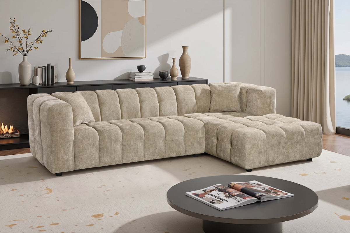 An L-shaped tufted sofa with right hand facing chaise end section, upholstered in beige chenille fabric, styled in a bright, modern living room