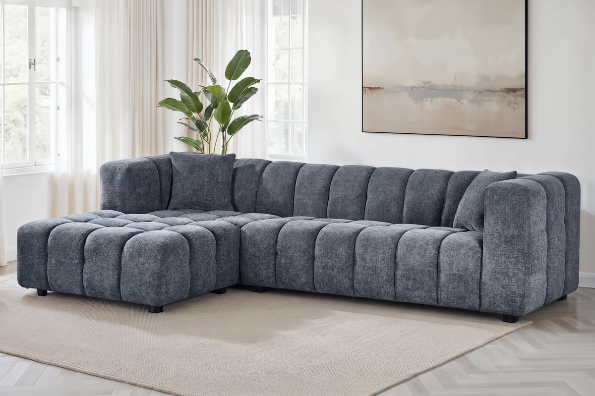 An L-shaped tufted sofa with left hand facing chaise end section, upholstered in pale blue chenille fabric, styled in a bright, modern living room