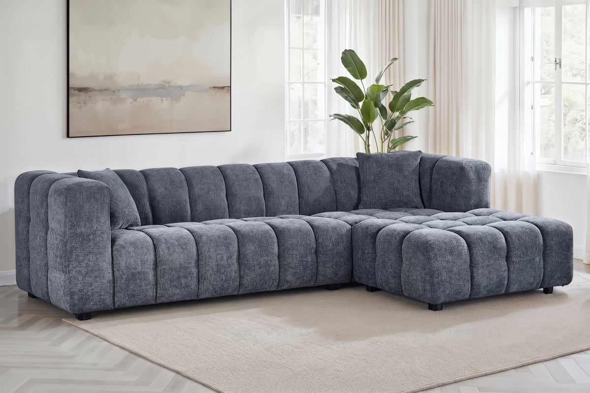 An L-shaped tufted sofa with right hand facing chaise end section, upholstered in pale blue chenille fabric, styled in a bright, modern living room