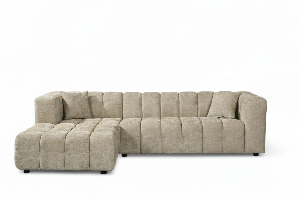 An L-shaped tufted sofa with left hand facing chaise end section, upholstered in beige chenille fabric
