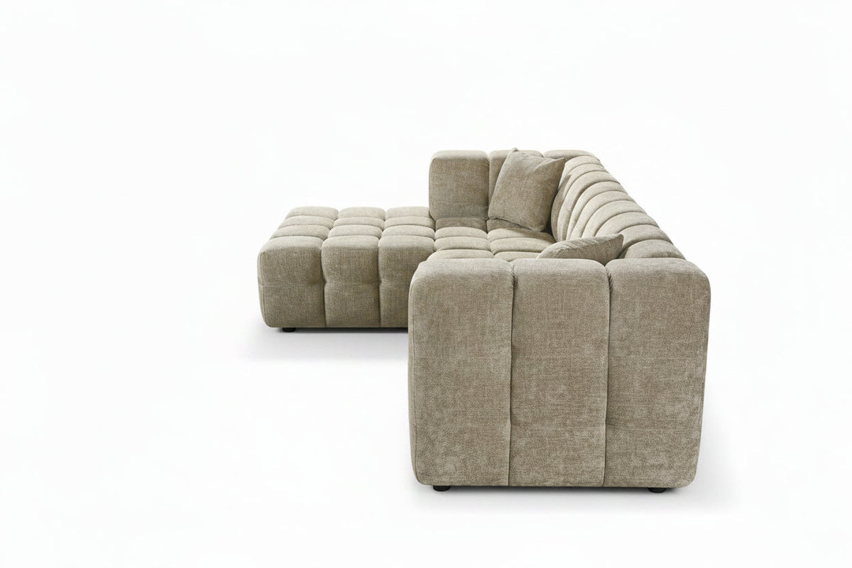 An L-shaped tufted sofa with left hand facing chaise end section, upholstered in beige chenille fabric