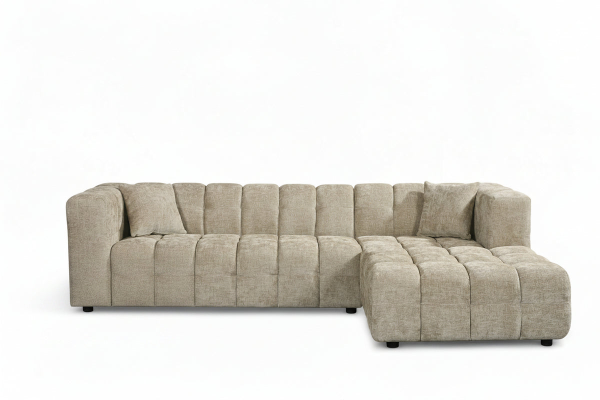 An L-shaped tufted sofa with right hand facing chaise end section, upholstered in beige chenille fabric