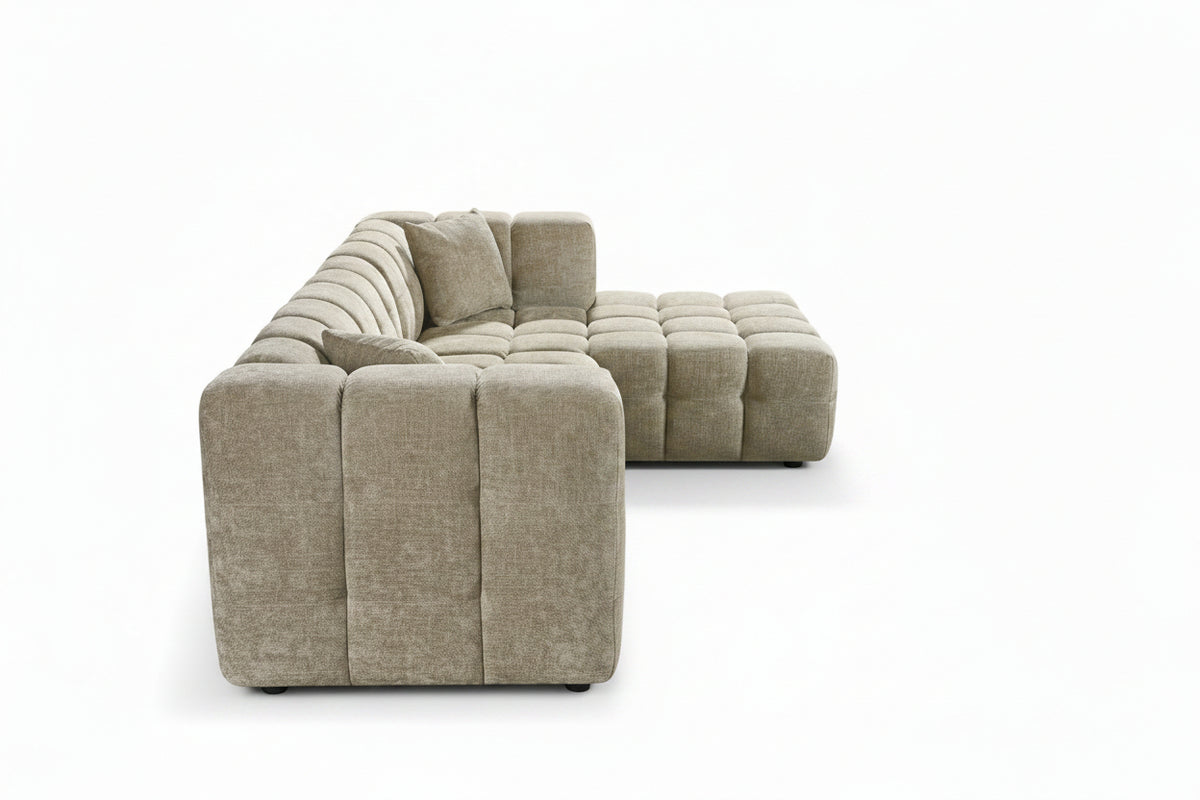 An L-shaped tufted sofa with right hand facing chaise end section, upholstered in beige chenille fabric