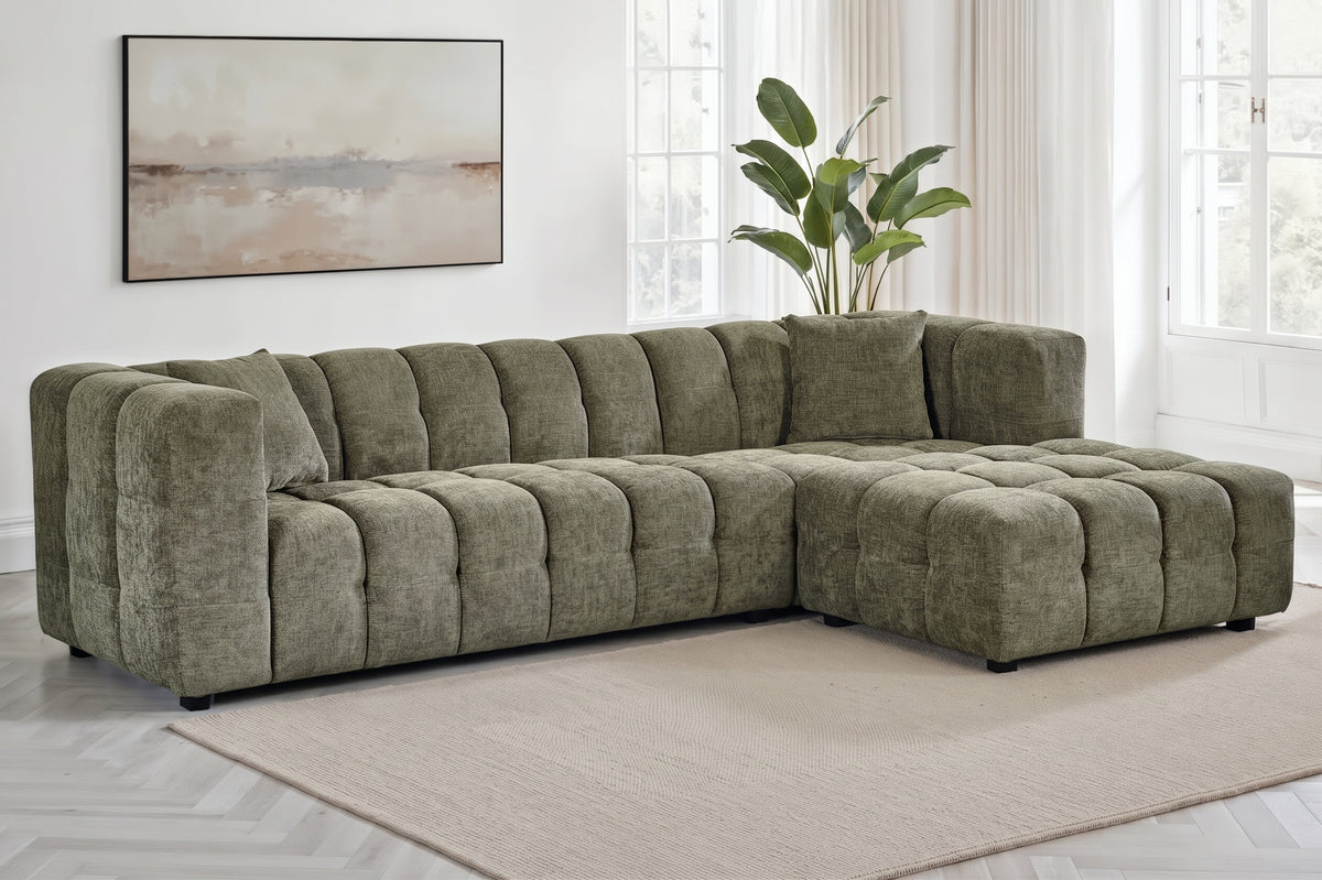 An L-shaped tufted sofa with right hand facing chaise end section, upholstered in textured sage green chenille fabric, styled in a bright, modern living room