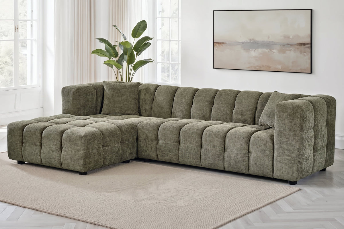 An L-shaped tufted sofa with left hand facing chaise end section, upholstered in textured sage green chenille fabric, styled in a bright, modern living room
